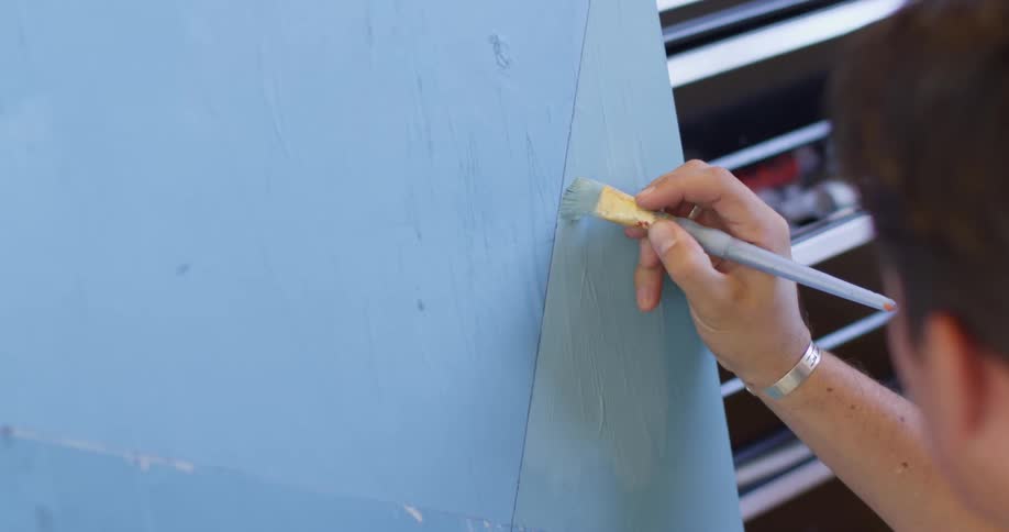 Man painting over canvas with blue paint using a small brush