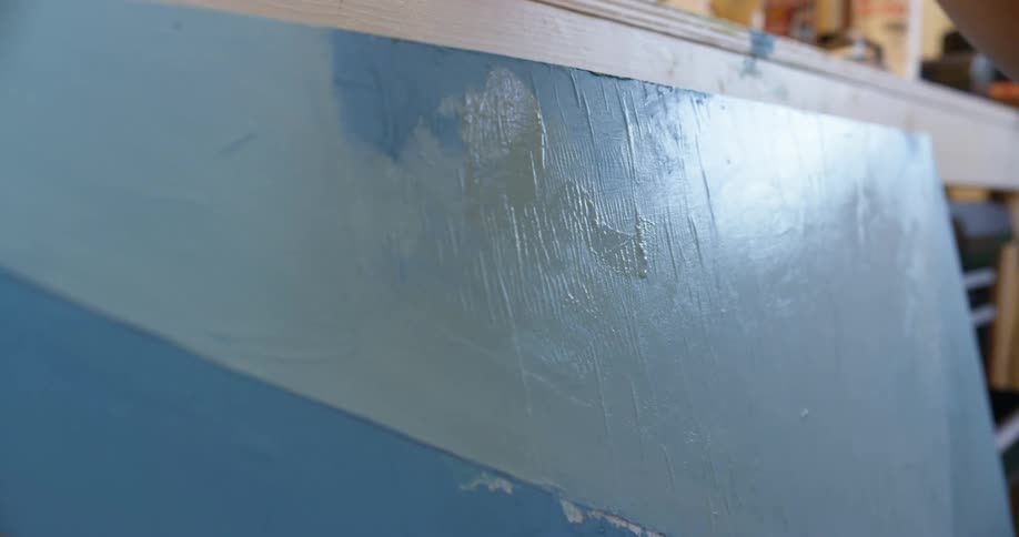 A woman adds splotches of white paint to a canvas already painted blue