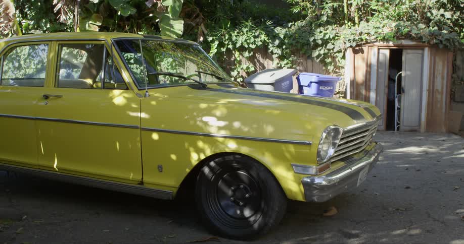 A yellow vintage vehicle is parked at an angle in a driveway
