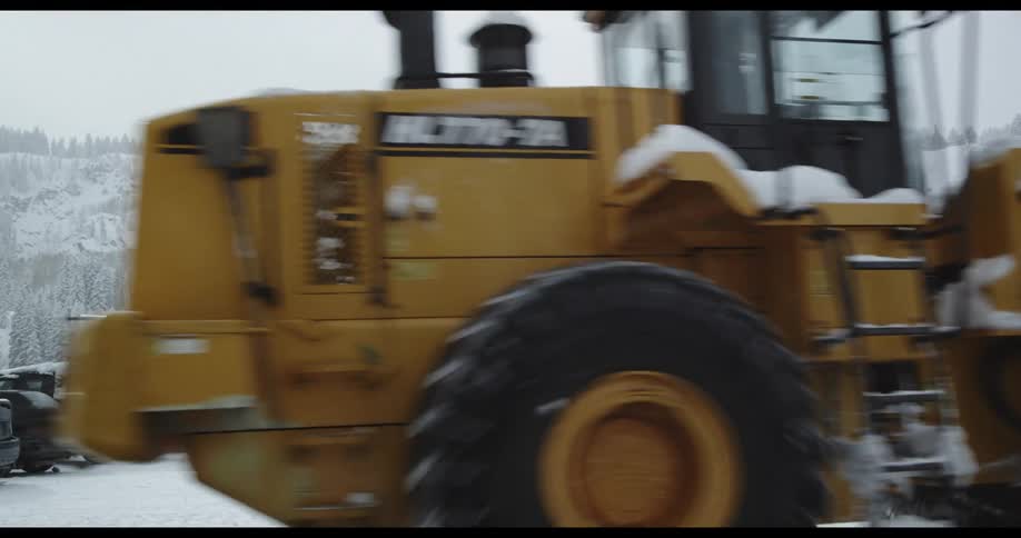 A tractor drives through a parking lot covered with snow with mountains in the background