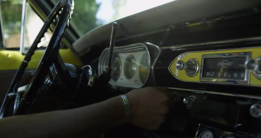 A person sitting in a car with a steering wheel puts the key in the ignition