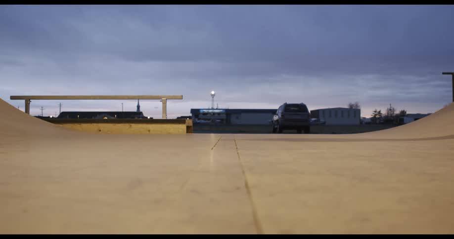 A person skating on a skateboard in a skate park with buildings the sky and clouds in the background