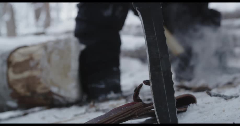 Man wearing winter clothes digs the frozen forest ground with a shovel