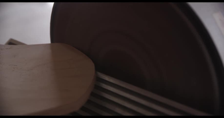 An oval shaped slab of wood being shaped on a machine indoors