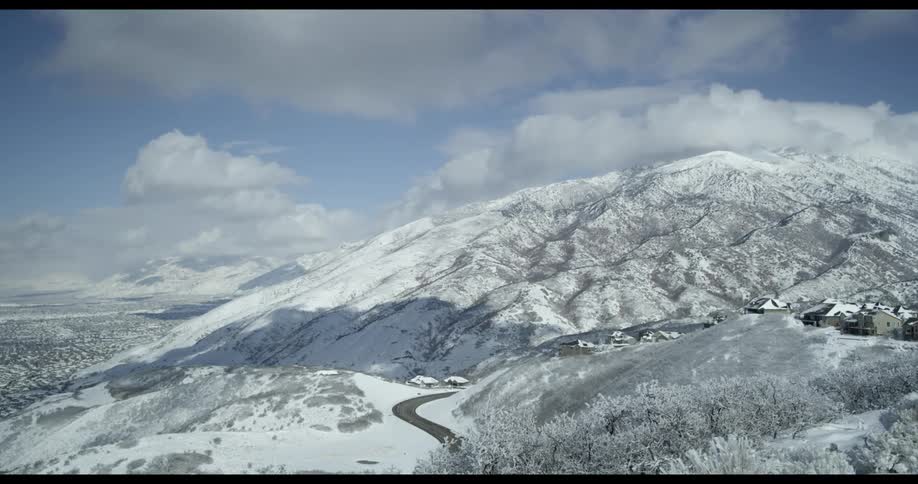 Snow covered mountain range with a winding road and a cloudy sky
