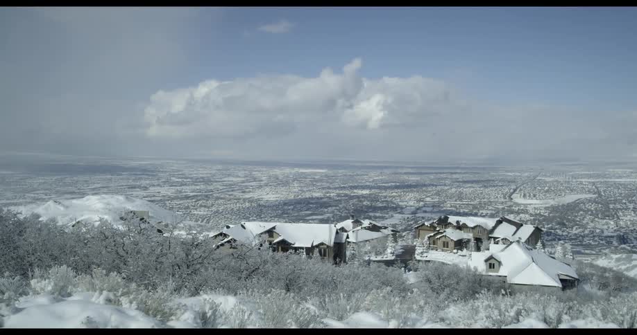 A group of snow covered buildings on a hill looming over a wintry countryside during the day