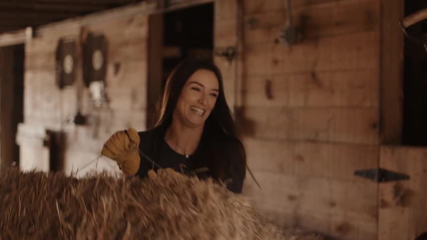 A man holding a saddle talking to a woman carrying a bale of hay