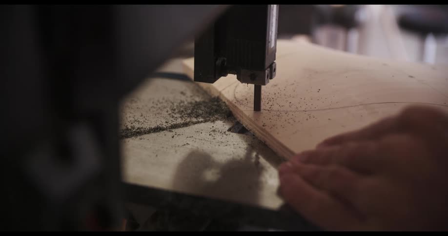 A person carefully guides a wooden board towards a band saw to cut it