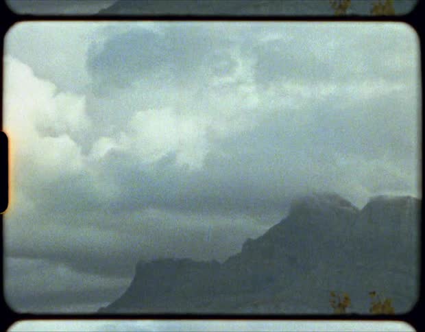 Thick clouds loom over a stone mountain ridge during the day