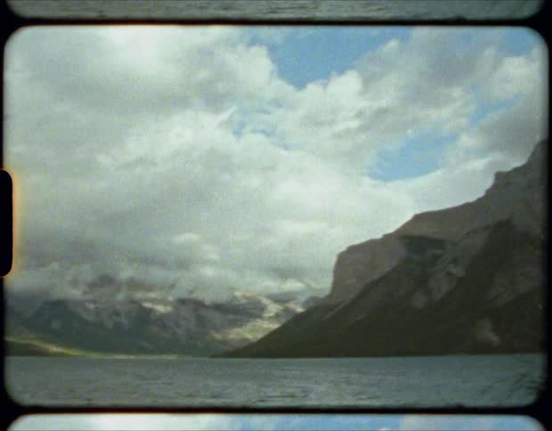 Film of the calm waters of a lake near the cloud covered peaks of a mountain range