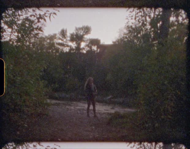 A woman skips stones across a river in a woodland during the day