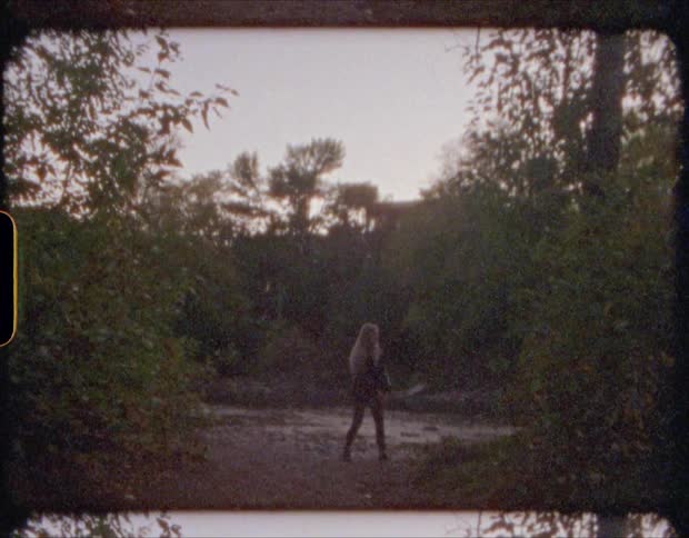 A woman skips stones across a river in a woodland in the evening
