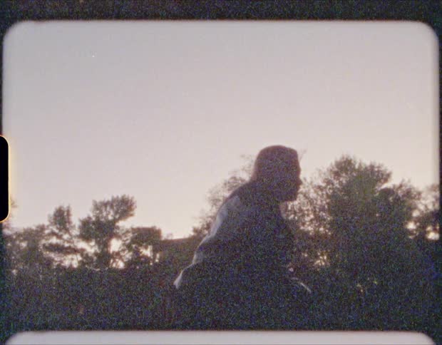 Blonde woman with a black leather jacket throws stones and is silhouetted against the sky at dusk