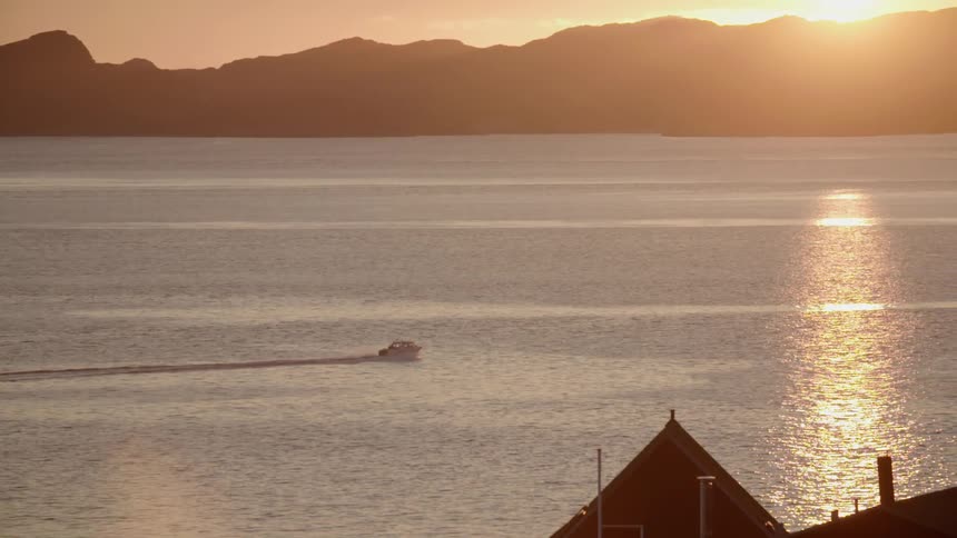 A boat is traveling along a lake at sunset