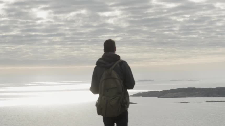 Man with backpack looking out at the ocean on a cloudy day