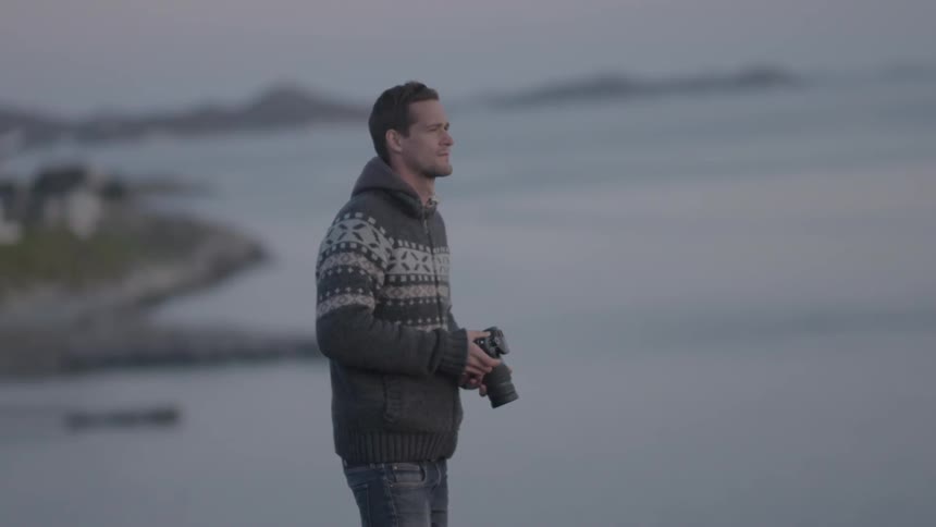 A man holding a camera as he overlooks a body of water