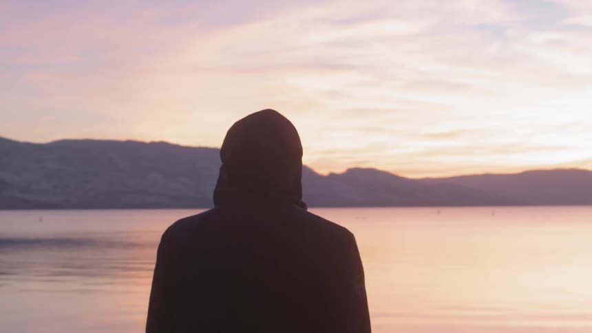 Man walking near a lake and looking at the orange sky after sunset