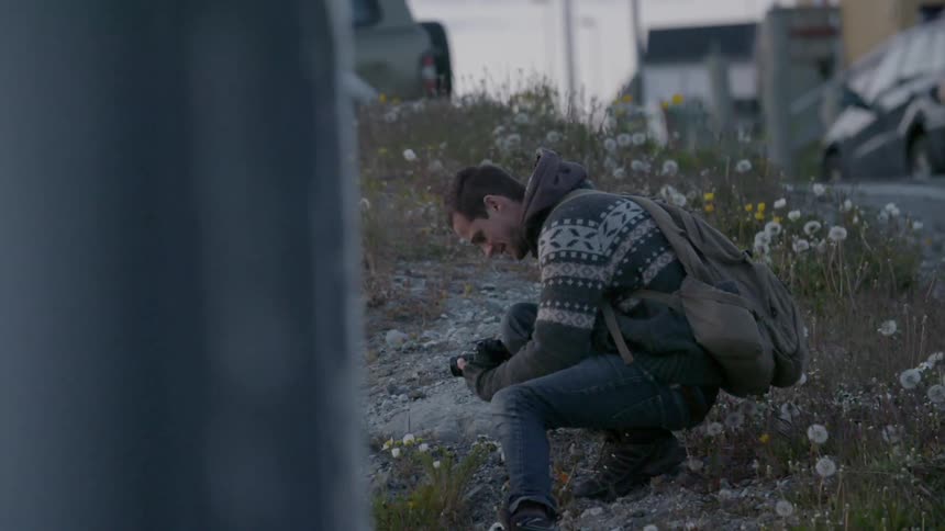Man with backpack kneeling down and looking at a camera
