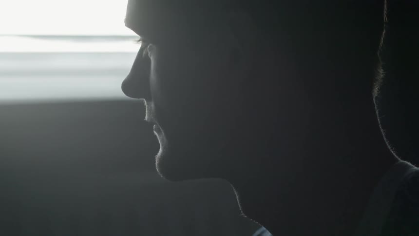 A man is standing in a dark area near a window