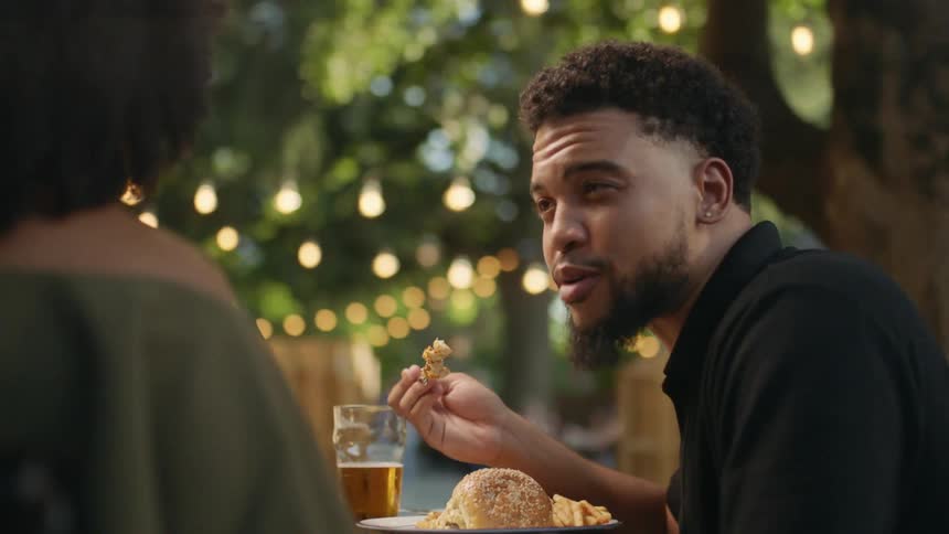 Man eating at a restaurant outdoors smiling and talking with woman on a date