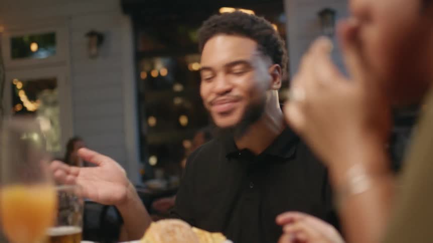 A man and woman laugh together sitting at an outdoor restaurant table