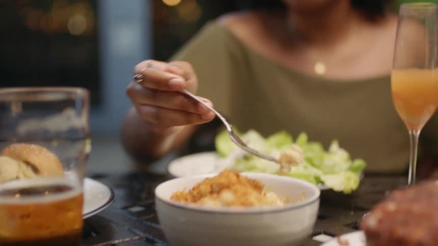 A woman retrieves food from a bowl in the center of a dining table in a restuarant with her fork before placing the food in her mouth