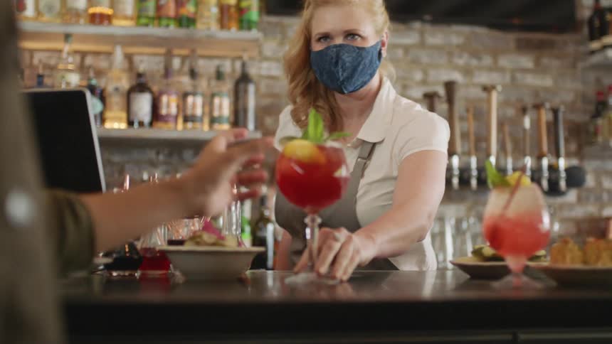 A bartender handing a drink to another person