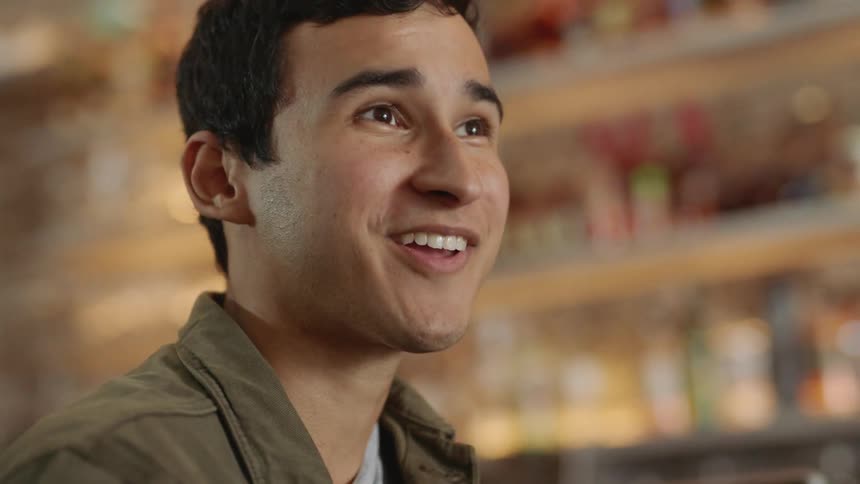 Man in front of a bar counter smiling and laughing to a friend off camera