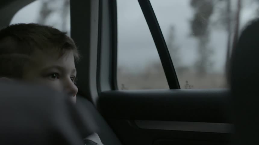 A child is sitting in the back of a moving car looking around