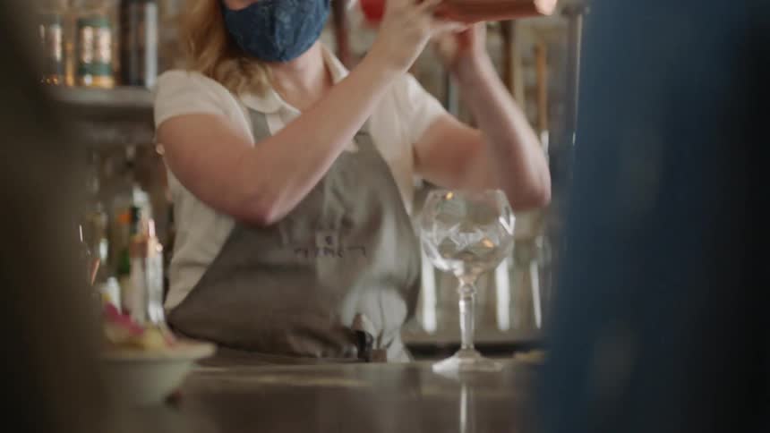 A bartender shaking a drink behind a bar counter in a restaurant for customers