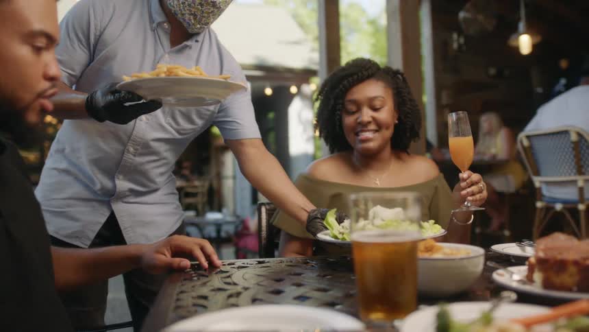 A waiter brings food to a man and woman sitting at a table with drinks at a restaurant