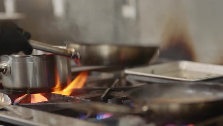 A person with gloves cooking on a stove with a pot and two frying pans
