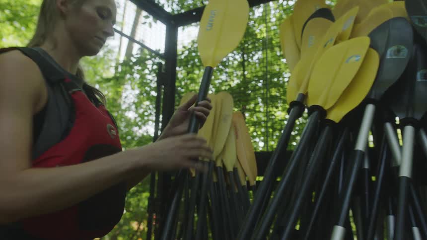 Woman selects kayaking paddle from a pile and walks off with it