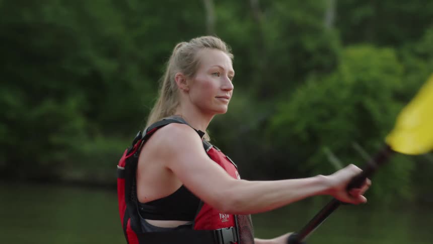A woman with a life jacket kayaking in a river with a paddle
