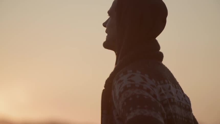 Man adjusting his sweater while standing at sunset