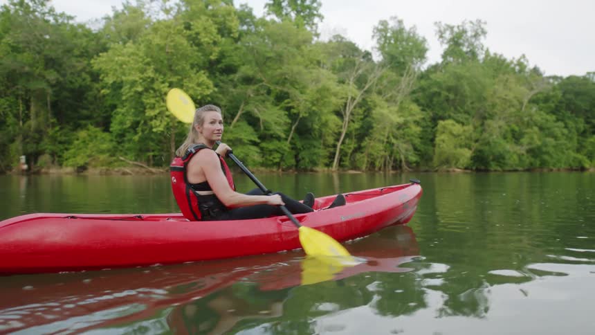 Woman in a red kayaking paddling with a yellow paddle stick down a river at daytime