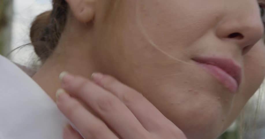 A young woman outside brushes her hair behind her ear