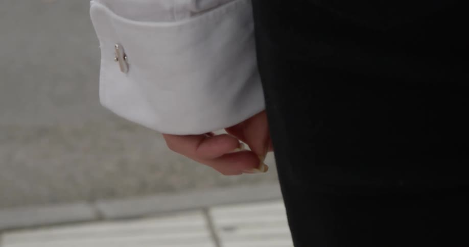 Hand of a woman moving around and picking at her finger nails standing outside
