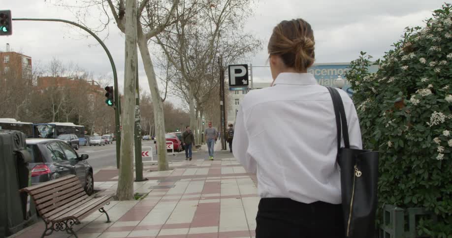 Woman walking on a sidewalk in a city next to parked cars in a parking lot
