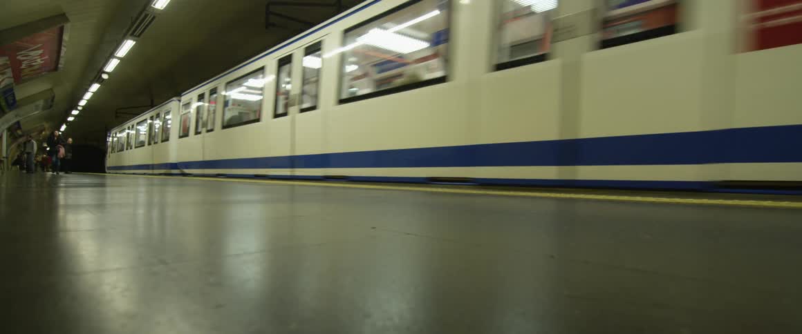 Two subway trains pass one another as people walk on the platforms nearby
