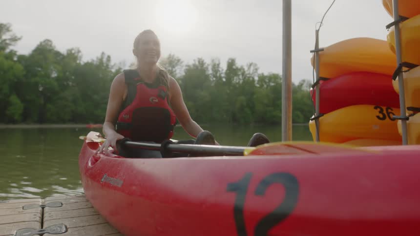 A woman in a safety vest sits in a canoe and holds on as the canoe is pushed into a lake