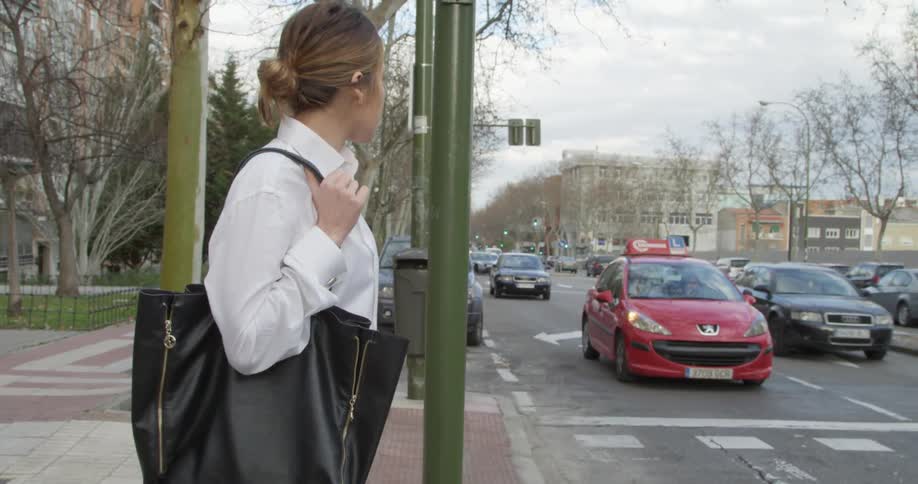 A woman stands on a sidewalk of a busy street with traffic as she watches