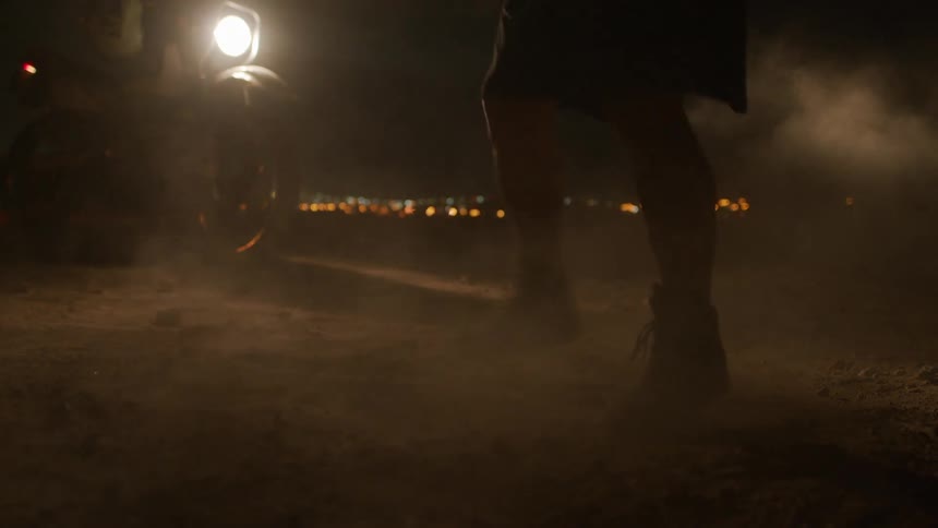 A man is jumping around at night by a motorcycle