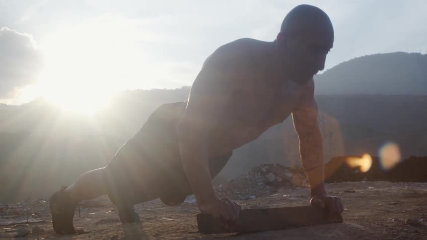 Man doing a push up outside in a junkyard at day time