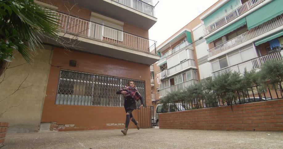 A woman completes a ballet jump outdoors on a patio during the day
