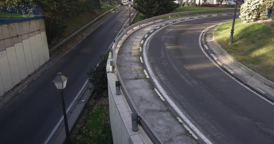 A curved road is slightly elevated from a lower road that a car drives along