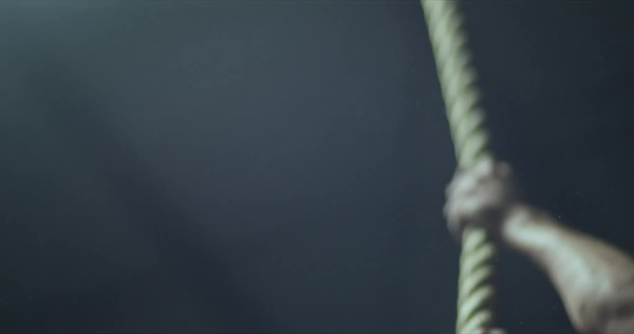 A man is climbing up a rope in a gym