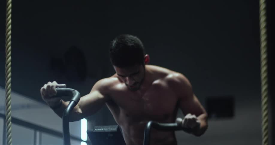 A muscular man pumps his arms as he pedals on an exercise bike