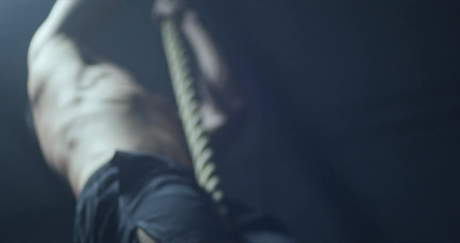 A man climbs up and a down a rope hanging from a ceiling as he wears black shorts