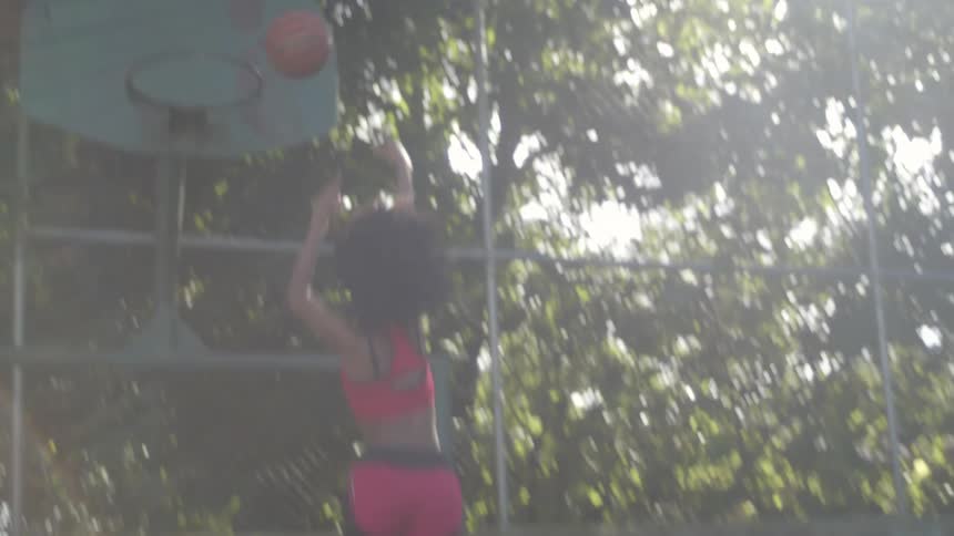 A woman playing basketball shoots a ball in to a hoop and makes a basket